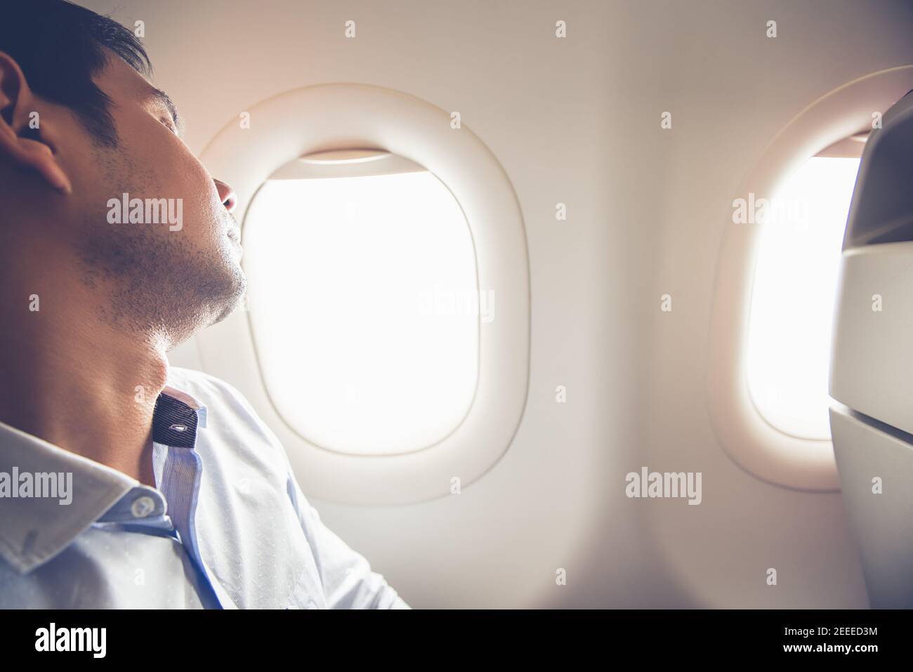 Müder Passagier schläft im Flugzeug am Fensterplatz Stockfoto