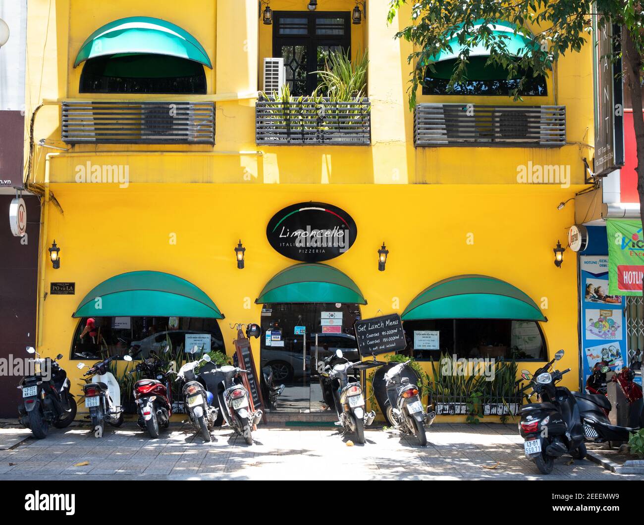 Danang, Vietnam - 27 Jul 2019: Gemütliches Café in gelbem Gebäude mit grünen Zelten und Motorrädern auf dem Parkplatz. Helles Äußeres des Cafés oder Cafés. Vietna Stockfoto