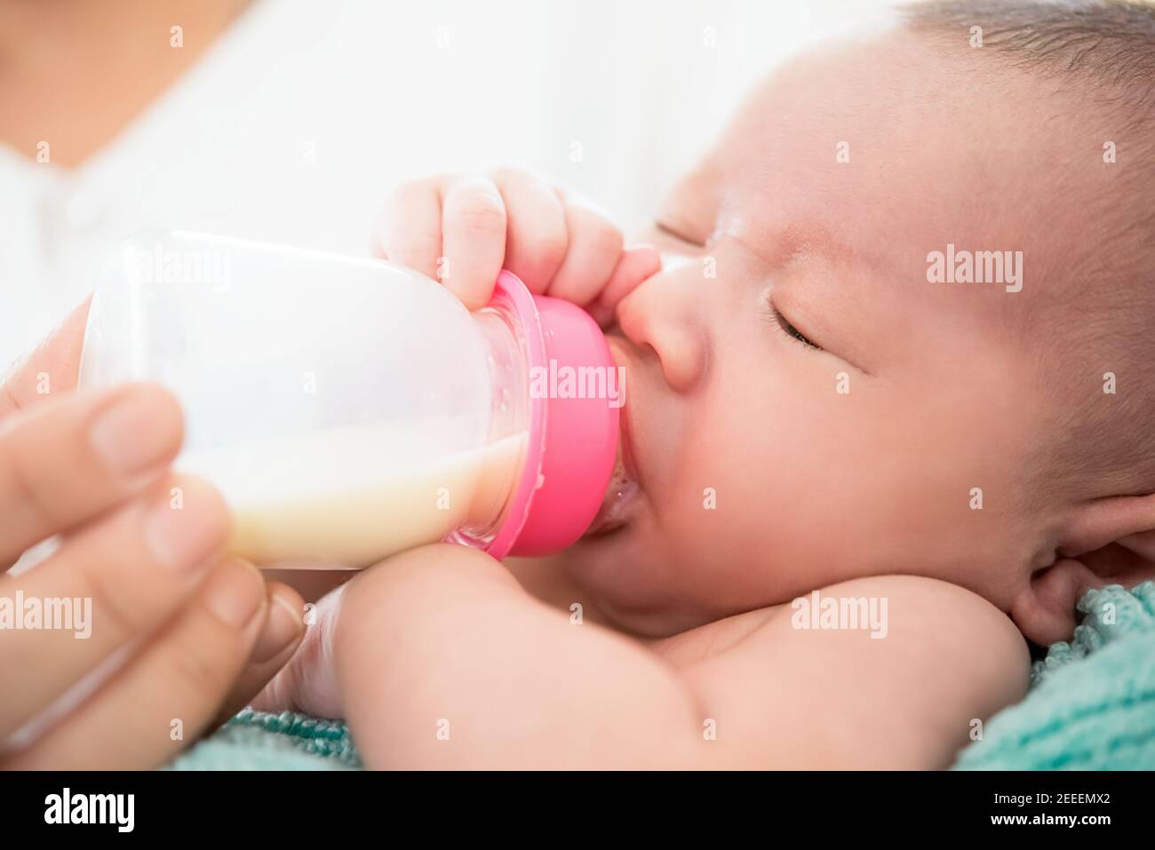 Schläfrig niedlichen Neugeborenen trinken Milch aus der Flasche in der Mutter Arme Stockfoto