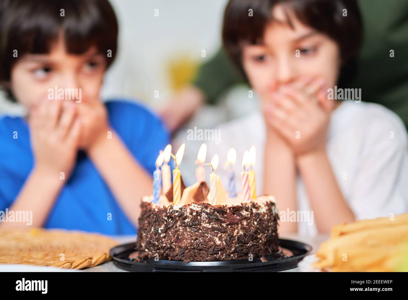 Zwei kleine hispanische Zwillinge, die Geburtstagskuchen angucken, während sie sich auf das Kerzenblasen vorbereiten. Lateinische Familie feiert Geburtstag zusammen zu Hause. Selektiver Fokus auf einen Kuchen Stockfoto