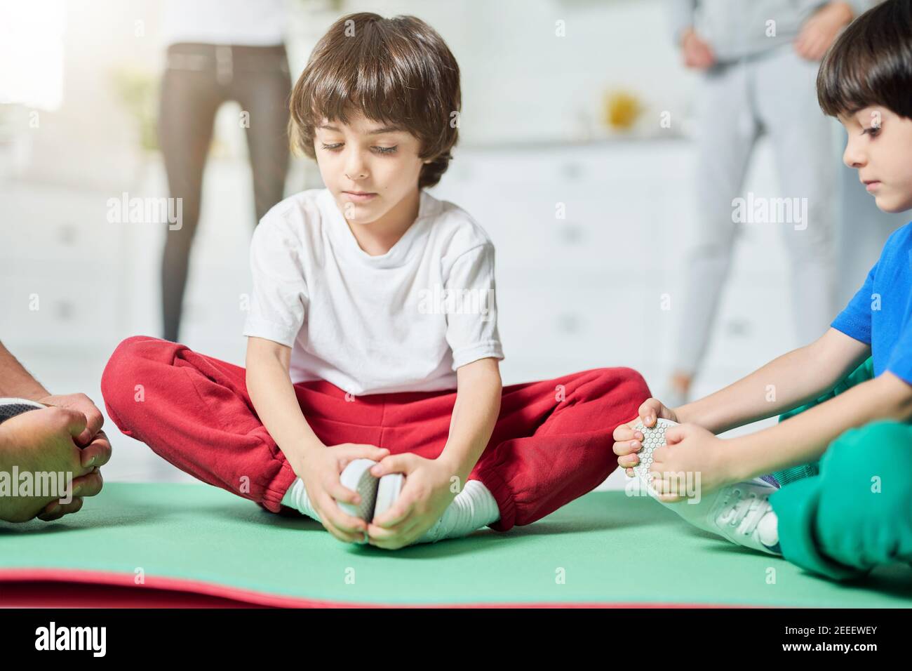 Zwei entzückende kleine hispanische Jungen sitzen in Yoga-Pose auf einer Matte, während mit den Eltern am Morgen Workout zu Hause. Kindheit, Sportkonzept Stockfoto
