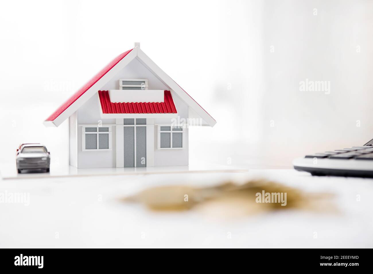 Haus Modell und Rechner auf dem Tisch mit Unschärfe Haufen Von Münzen im Vordergrund - Immobilien Finanzkonzept Stockfoto