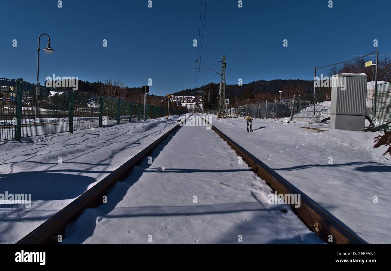 Abnehmende Perspektive von schneebedeckten Eisenbahnschienen mit Oberleitung von Zäunen umgeben an sonnigen Wintertag mit blauem Himmel umgeben. Stockfoto