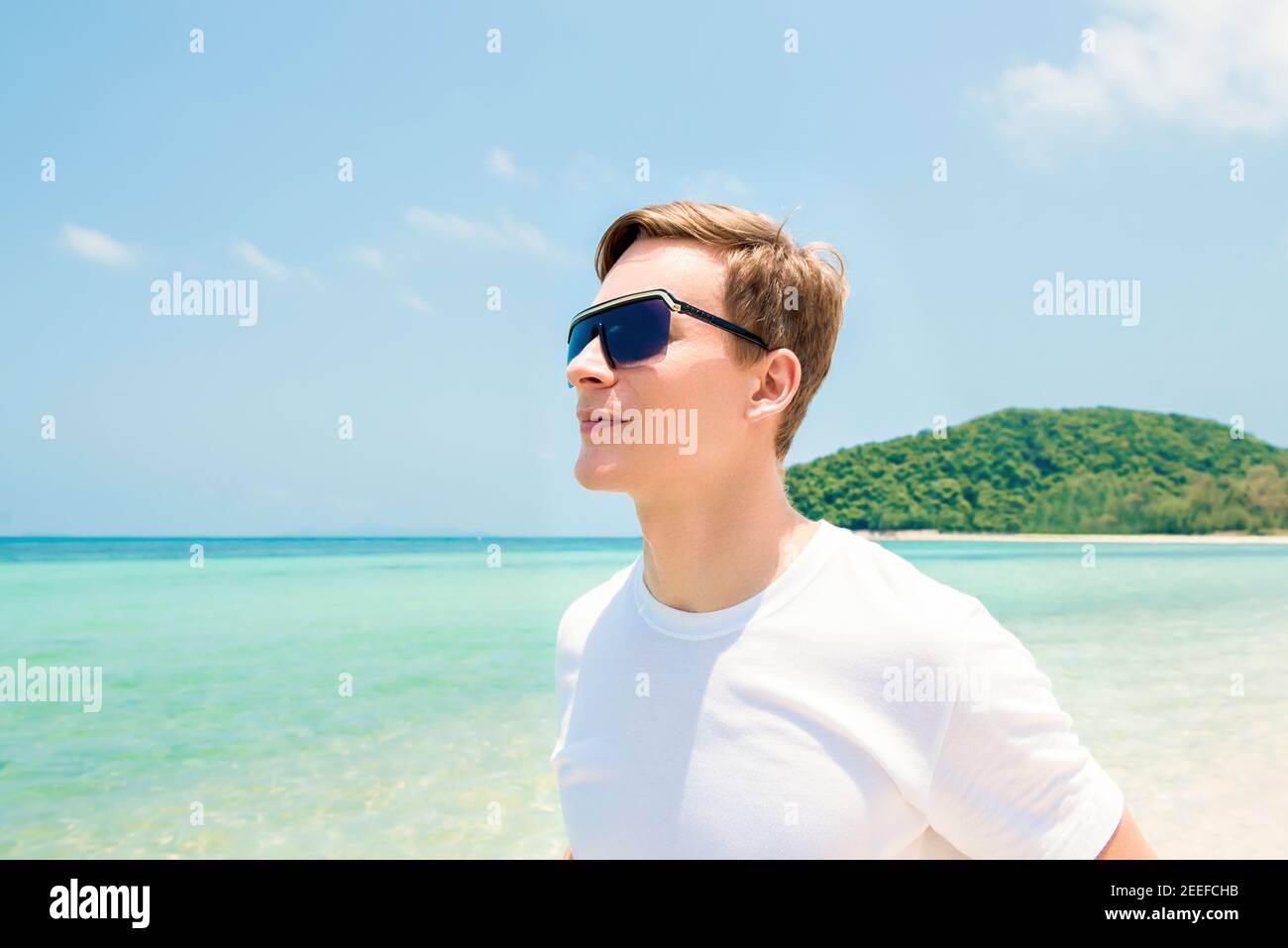 Männlicher Tourist mit Sonnenbrillen, der im Sommer am Strand steht Stockfoto