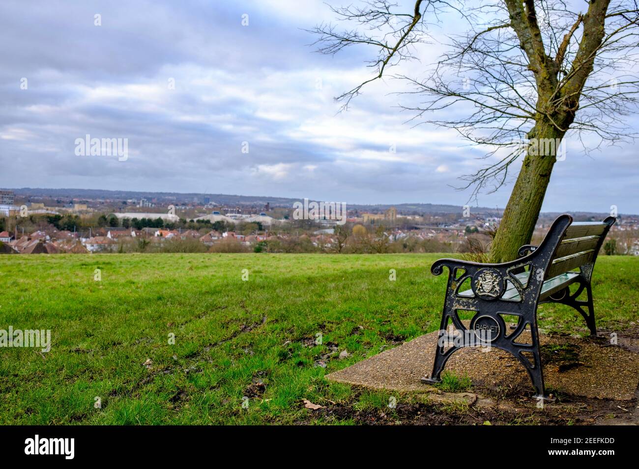 Eine Parkbank, auf der Barnett eingraviert ist, im Sunny Hill Park, Hendon, mit Blick auf North West London, Großbritannien. Ein wolkiger Wintertag. Stockfoto