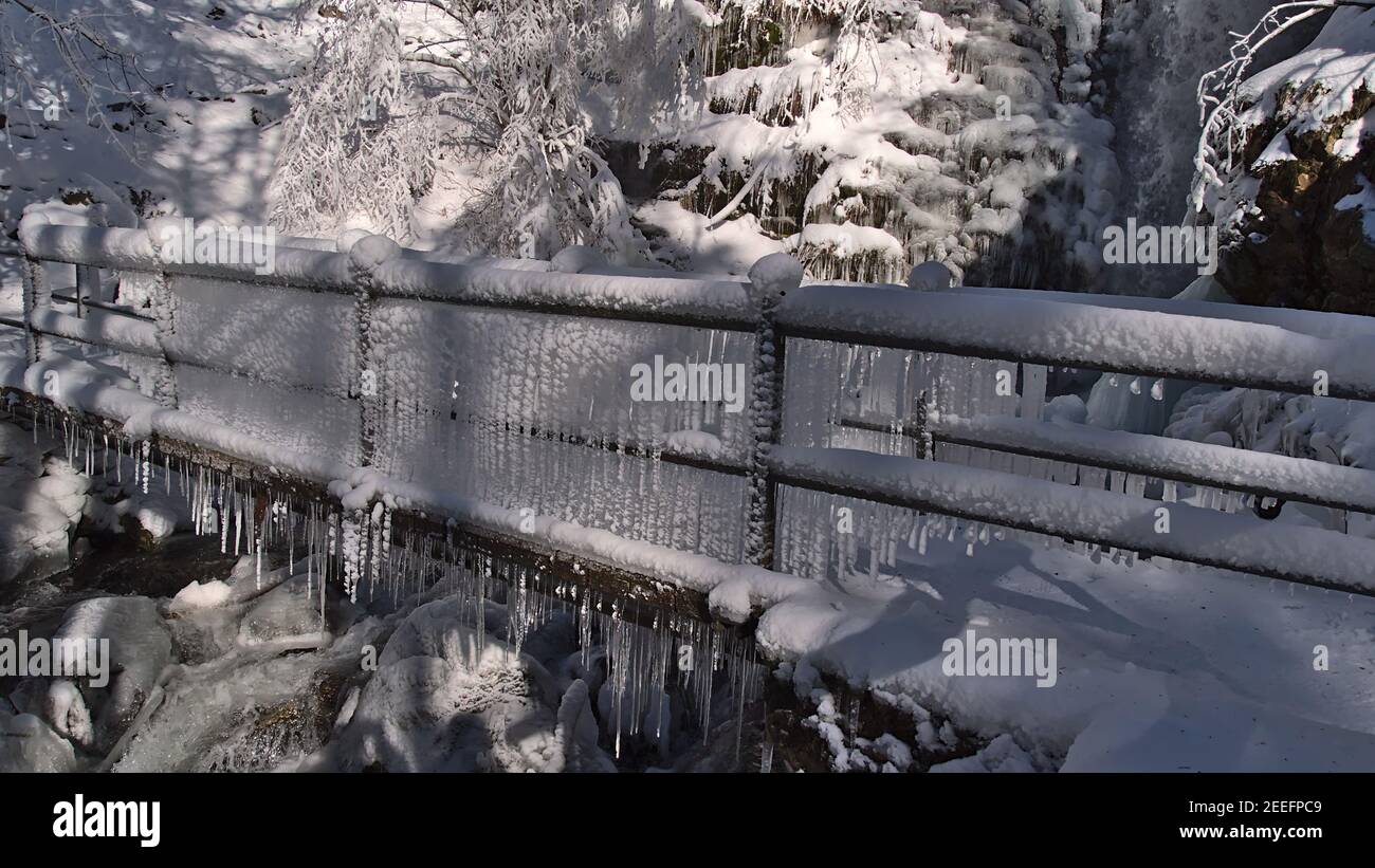 Bizarr aussehende gefrorene Brücke voller Eiszapfen mit Bach und Wasserfall Todtnauer Wasserfälle im Hintergrund in schneebedeckten Wald an sonnigen Wintertag. Stockfoto
