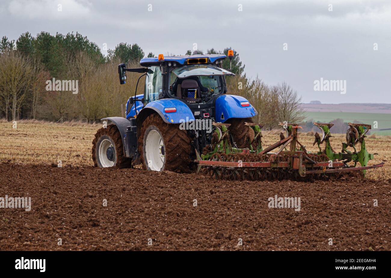 New Holland Traktor kultiviert ein dunkelrotes Schlammfeld Winter Stockfoto
