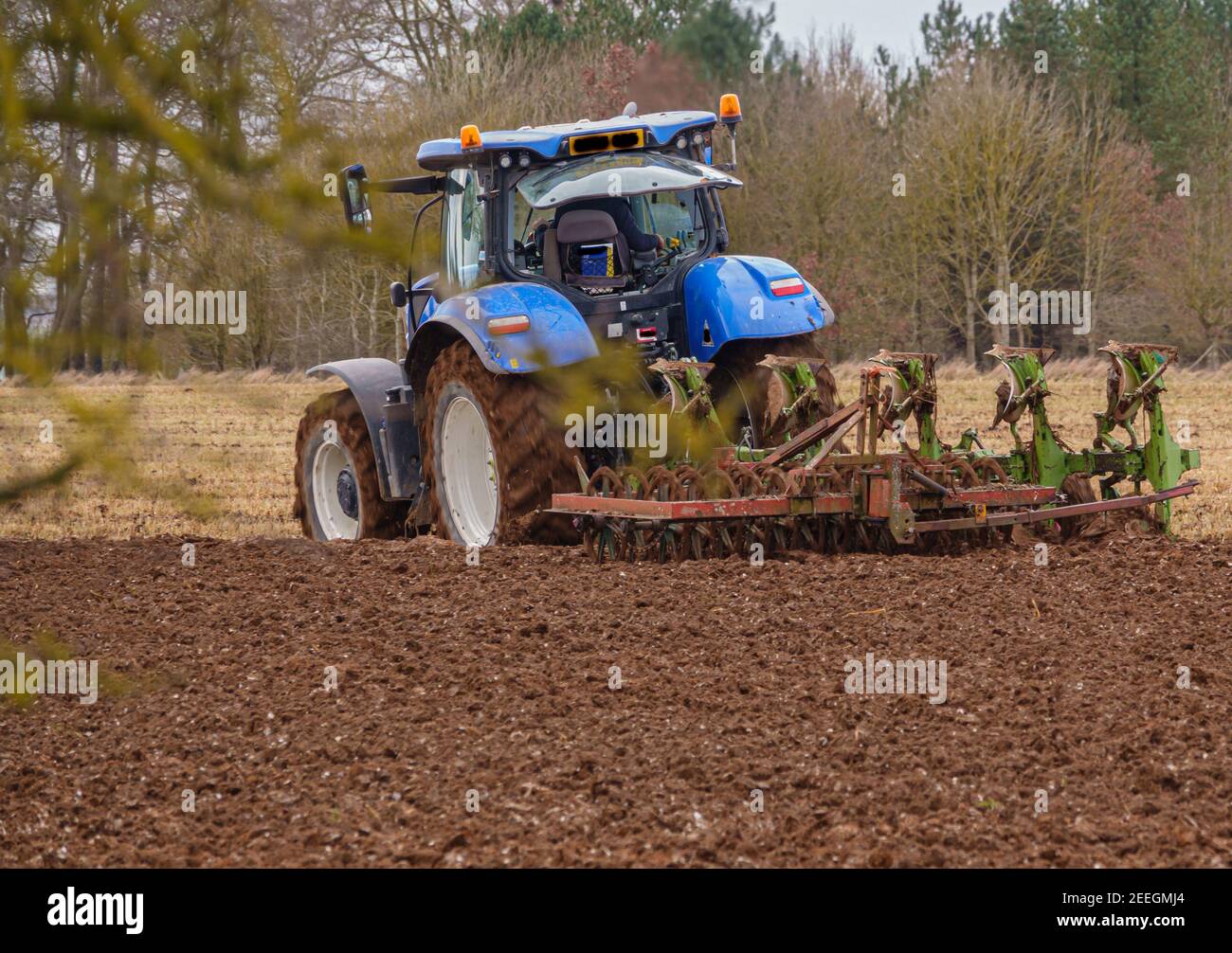 New Holland Traktor kultiviert ein dunkelrotes Schlammfeld Winter Stockfoto