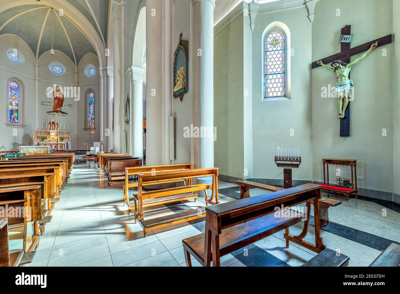 Blick auf Kreuz und Kirchenbänke im Kirchenschiff von Divin Maestro - einer römisch-katholischen Pfarrkirche in Alba, Italien. Stockfoto