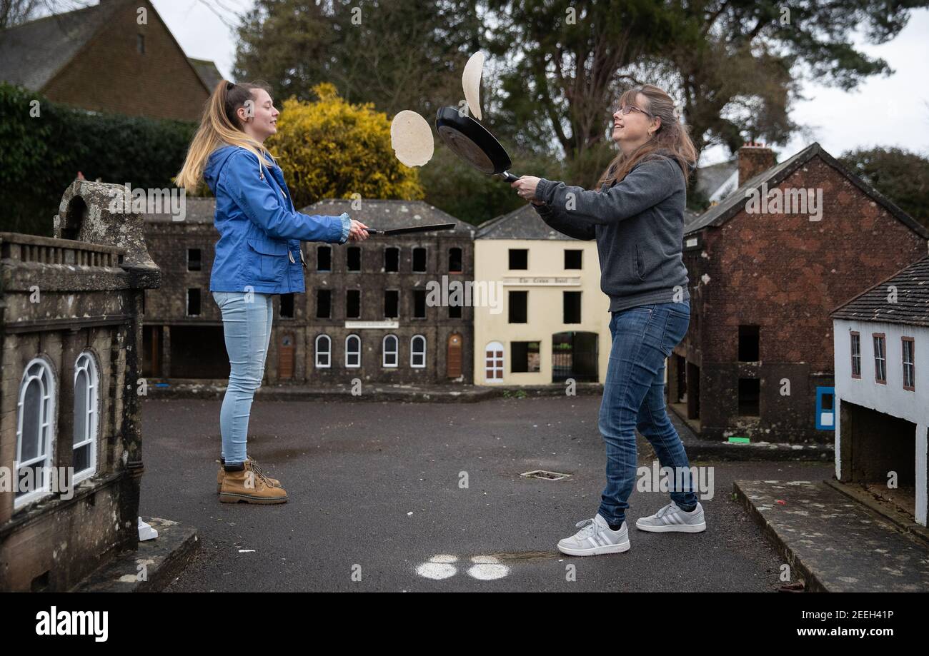 Mutter und Tochter Freiwillige Niki (rechts) und Rachel üben ihre Pfannkuchen werfen in den Straßen von Wimborne Modellstadt und Gärten, während sie am Wimborne Minster virtuellen Pfannkuchen Rennen teilnehmen. Bilddatum: Dienstag, 16. Februar 2021. Stockfoto