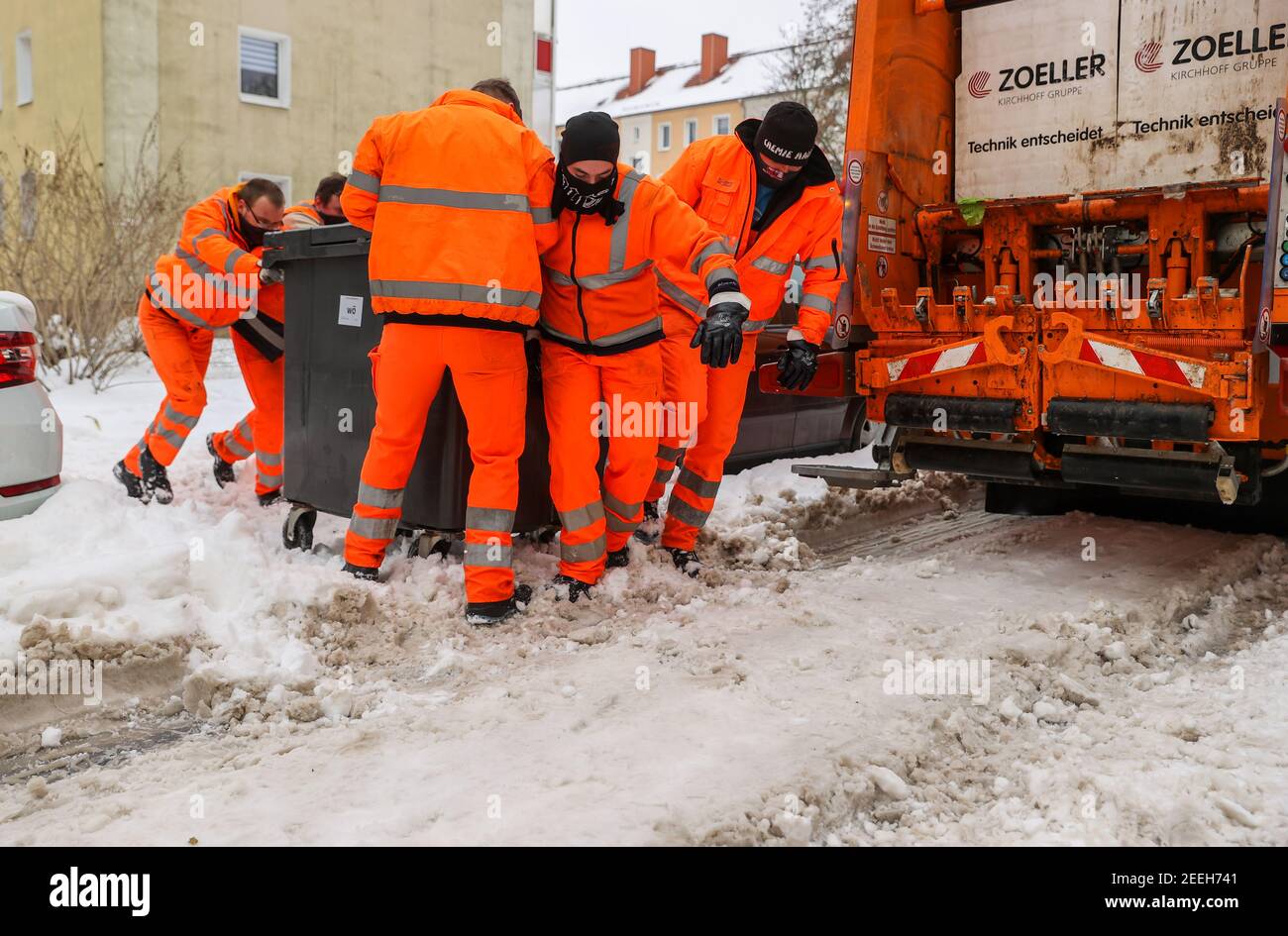 Sachsen-Anhalt, Halle Saale, 16. Februar 2021, sechs Mitarbeiter der Stadtwerke Halle versuchen, einen Abfallcontainer durch den Tiefschnee zum Fahrzeug zu ziehen. Aufgrund der aktuellen Wetterlage müssen sich die Mitarbeiter des Wasserversorgungsunternehmen Halle (HWS) mit schwierigeren Herausforderungen auseinandersetzen. In einigen Fällen müssen die vollen Abfallbehälter zwischen geparkten Autos, Schnee und Eis auf die Straßen gezogen werden. Foto: Jan Woitas/dpa-Zentralbild/dpa Stockfoto