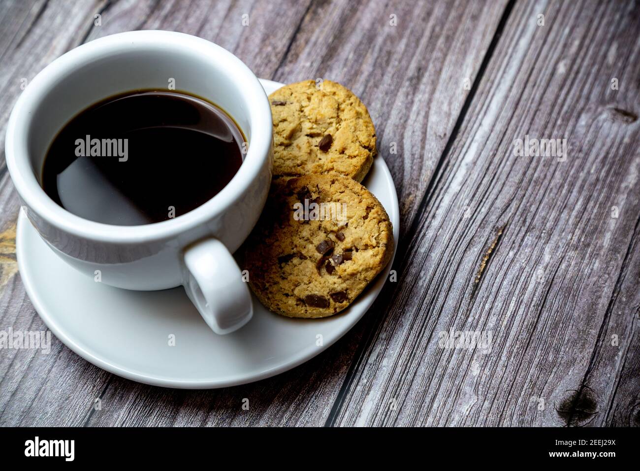 Chocolate Chip Cookies neben einer Tasse Kaffee Eine Untertasse auf einem rustikalen Holztisch Stockfoto