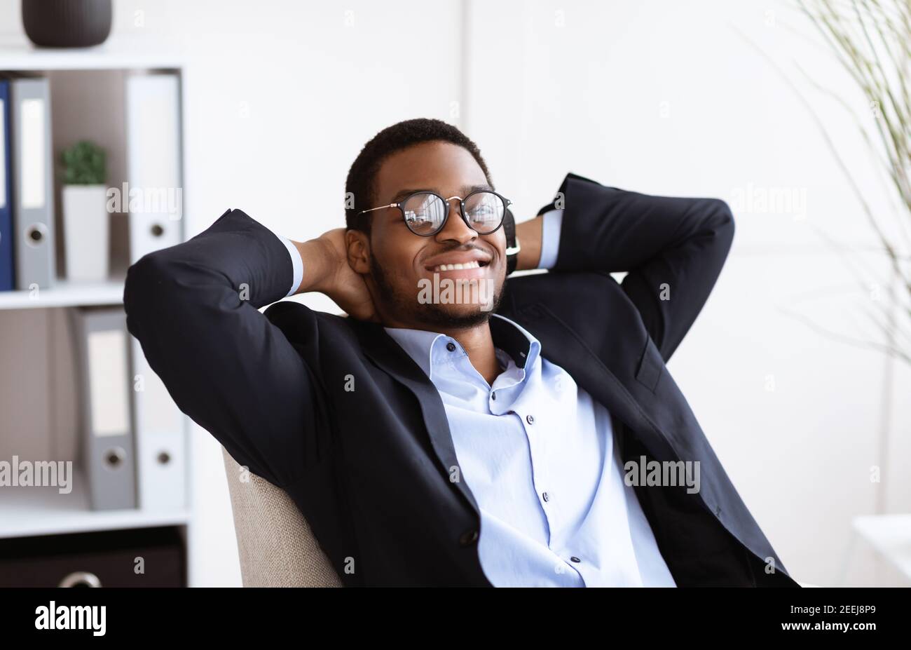 Fröhlicher schwarzer Geschäftsmann, der in seinem Schrank auf einem Stuhl liegt Stockfoto
