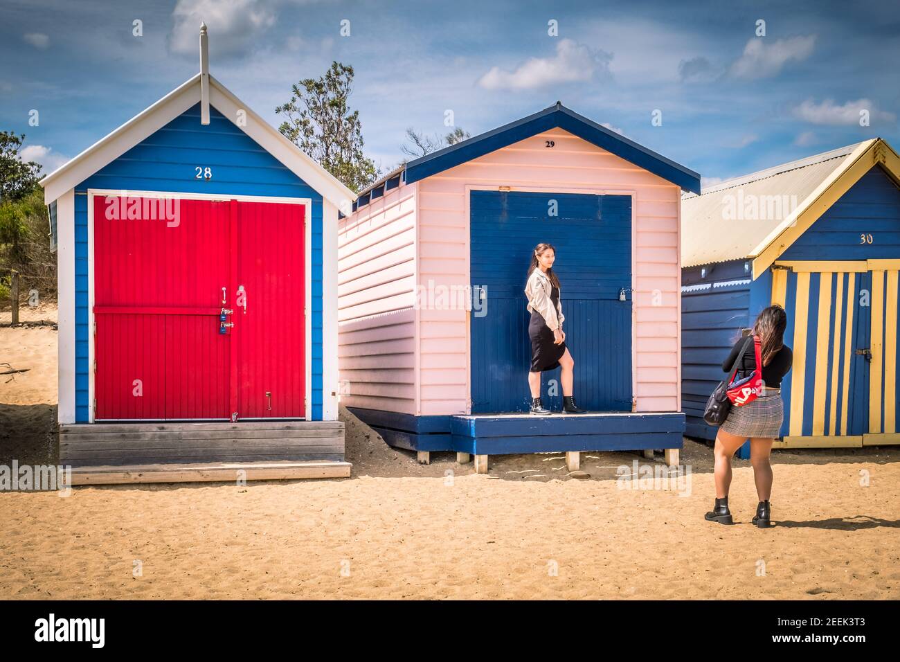 Eine Person fotografiert eine andere vor einem farbenfrohen Strand am Brighton Beach in der Nähe von Melbourne, Australien Stockfoto