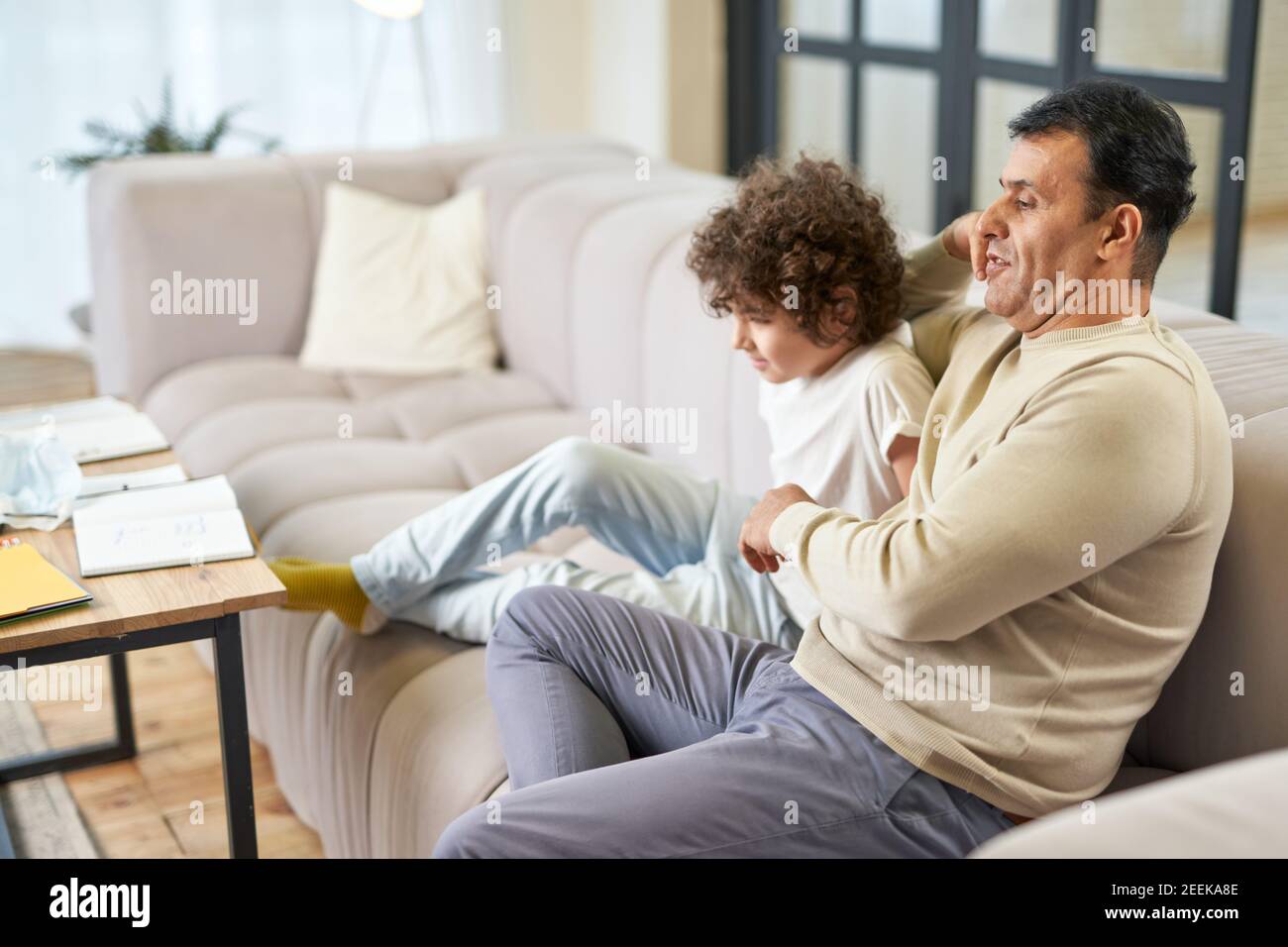 Glücklicher lateinischer Vater mittleren Alters, der Zeit mit seinem Sohn verbringt, Fernsehen im Wohnzimmer zu Hause. Familie, Freizeit, Vaterschaft Konzept Stockfoto