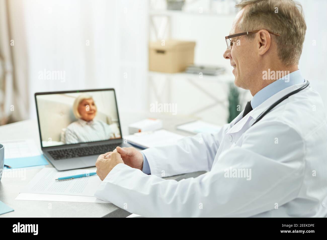 Fröhliche Arzt, der Online-Beratung für alte Frau in der Klinik Stockfoto