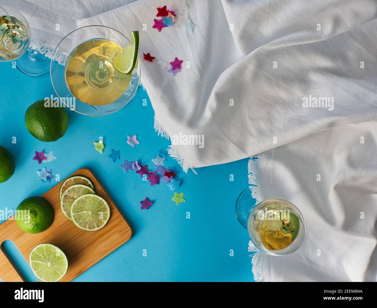 Gläser Wein und Spirituosen auf weißem, zerknittertem Tuch mit blauem Hintergrund, Tisch mit geschnittenen Limettenscheiben und Reststücken Stockfoto