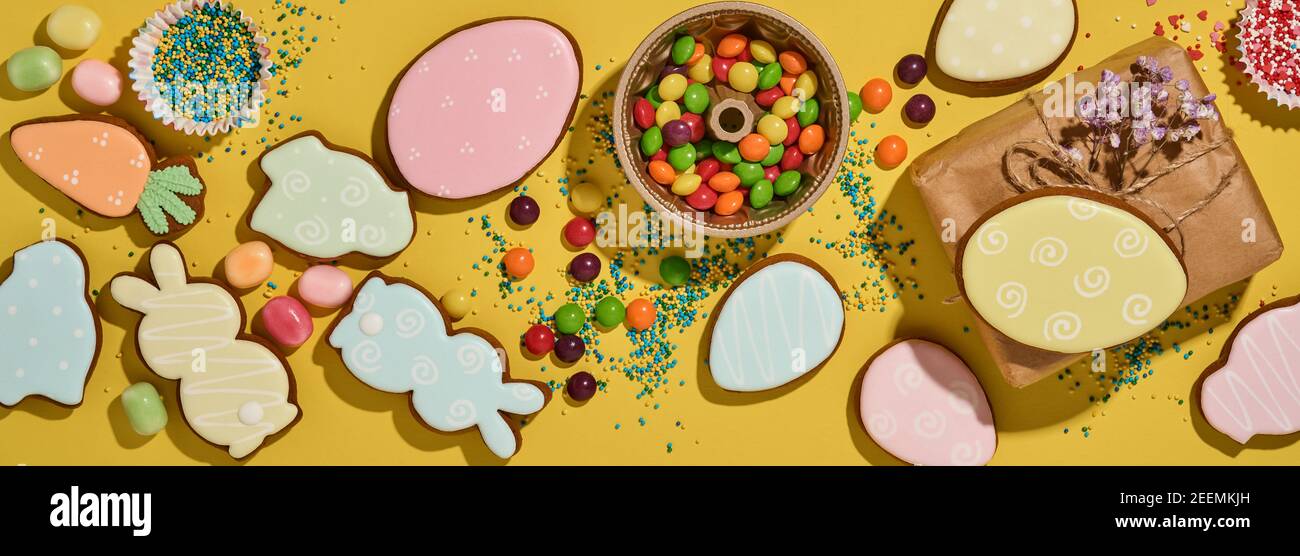 Ostern Backen Hintergrund. Ostern bunten Lebkuchen, Süßigkeiten, verstreute Süßwaren Topping Dressing und Geschenkbox auf gelbem Hintergrund. Feiern Stockfoto
