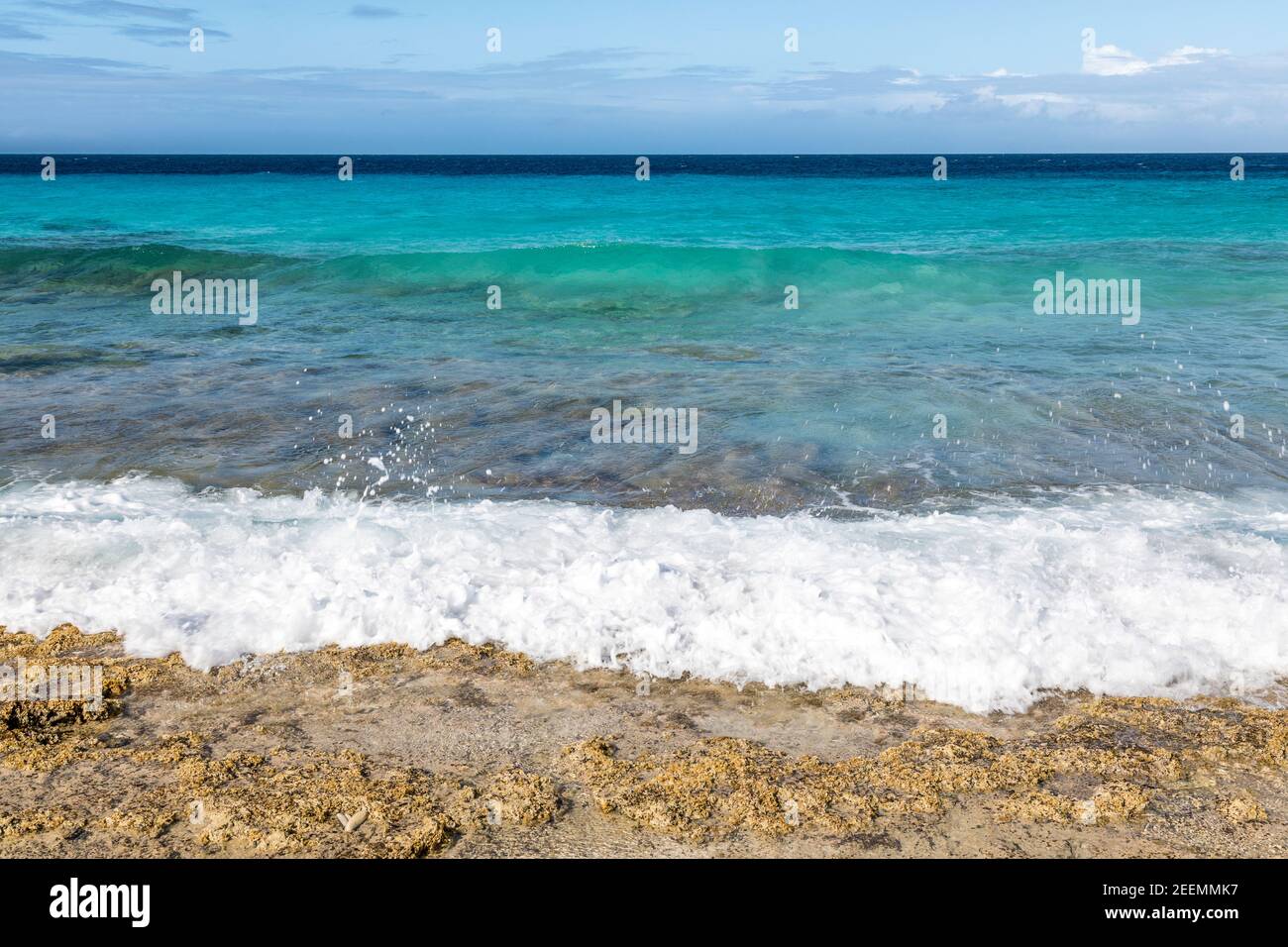 Kristallklares aquamarinfarbenes Meer mit Wellen, die in die Sonne brechen Korallenstrand bei den Sklavenhäusern auf der Karibikinsel Von Bonaire Stockfoto