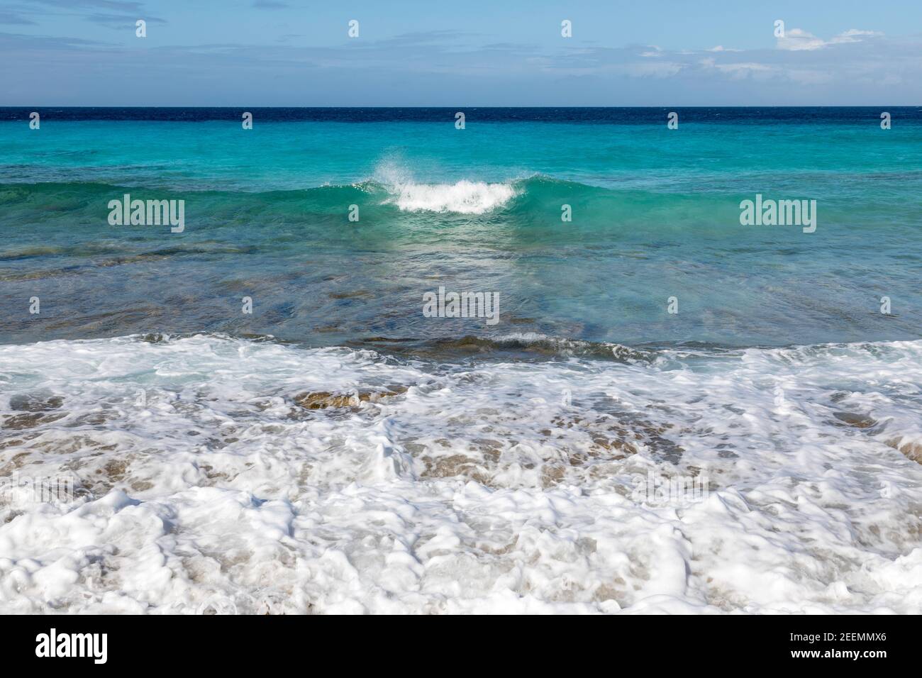 Kristallklares aquamarinfarbenes Meer mit Wellen, die in die Sonne brechen Korallenstrand bei den Sklavenhäusern auf der Karibikinsel Von Bonaire Stockfoto