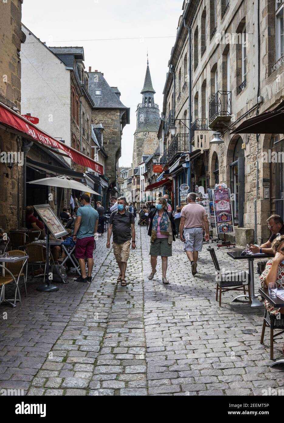 Menschen, die in trübseliger Sonne entlang einer gepflasterten Straße spazieren, Open-Air-Cafés in der Altstadt von Dinan, Frankreich, tragen Gesichtsmasken wegen der Pandemie Stockfoto