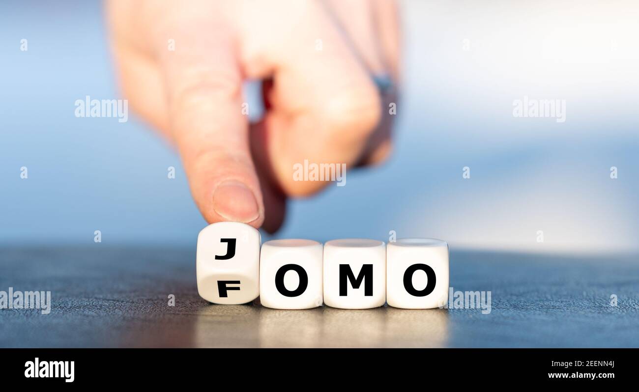 Hand dreht Würfel und ändert die Abkürzung FOMO (Fear of missing out) in JOMO (Joy of missing out). Stockfoto