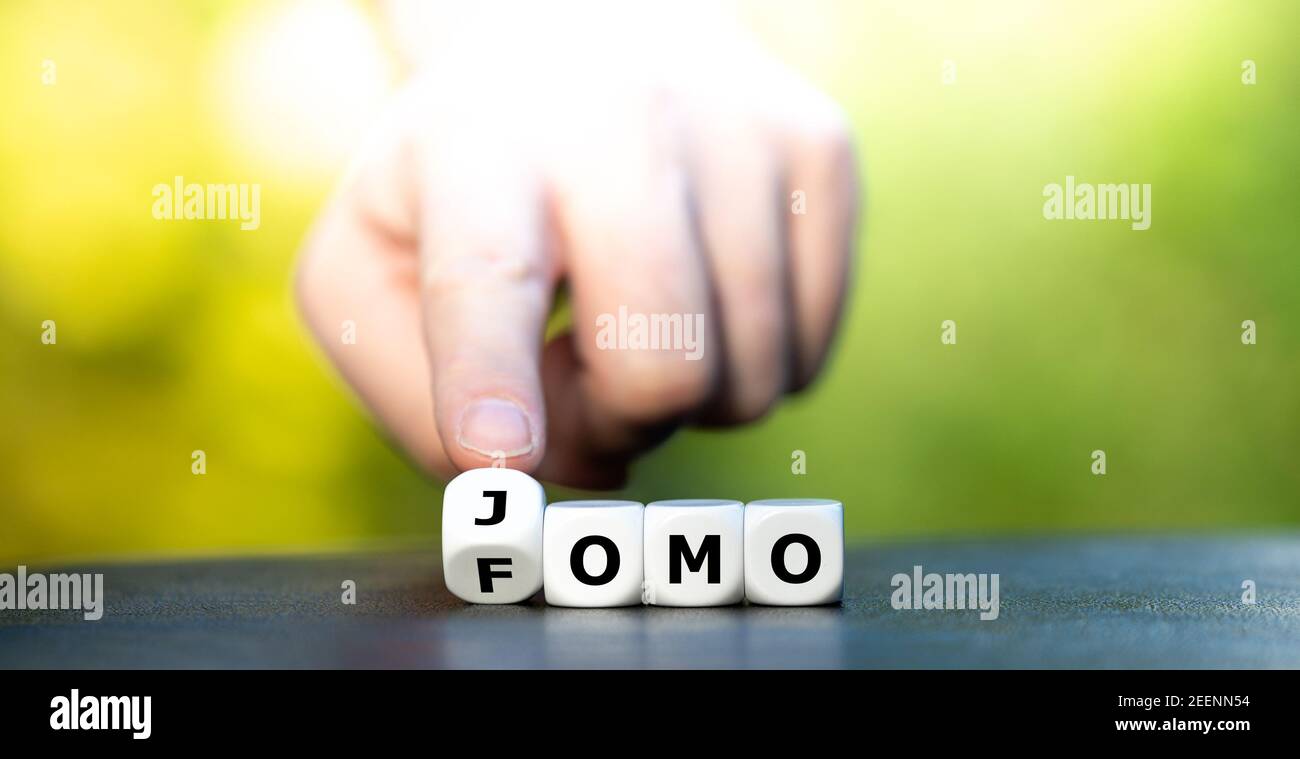 Hand dreht Würfel und ändert die Abkürzung FOMO (Fear of missing out) in JOMO (Joy of missing out). Stockfoto