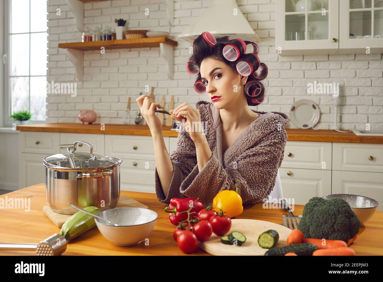 Wütend junge Frau in Haar Lockenwickler sitzen am Küchentisch, Feilen Nägel und Denken Stockfoto