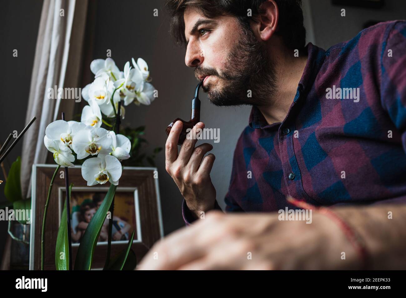 Ein Mann in seinen 40s Jahren schaut aus einem Fenster und raucht eine Pfeife. Konzept von Bein Stockfoto