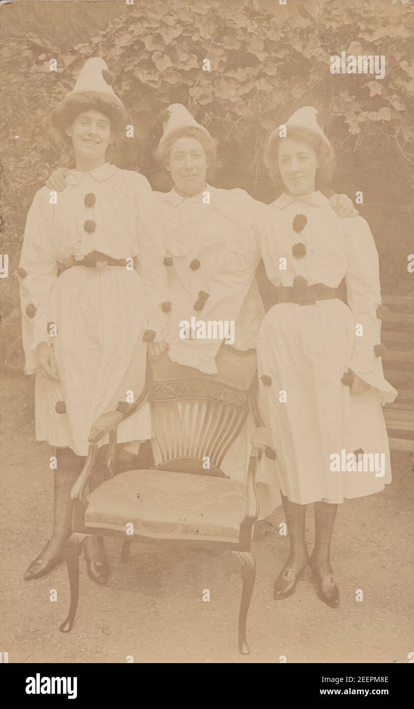 Jahrgang Anfang 20th Jahrhundert Foto Postkarte zeigt drei Frauen verkleidet als Pierrots. Stand hinter einem Stuhl im Garten. Stockfoto