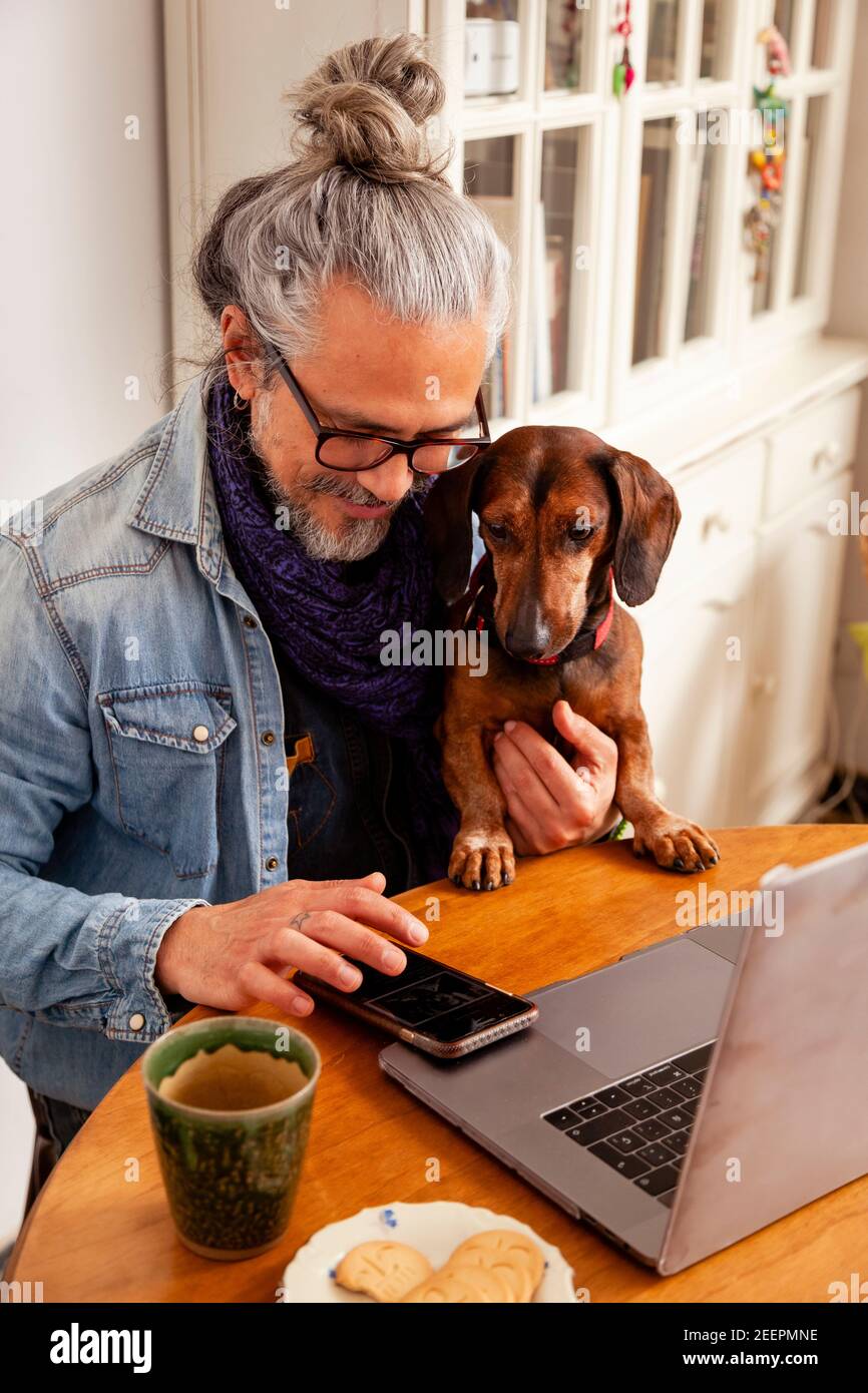 Schöner Mann, der zu Hause mit Laptop auf dem Tisch arbeitet, zusammen mit seinem niedlichen Hund; Konzept: Enge Beziehung zwischen Hund und Mensch Stockfoto