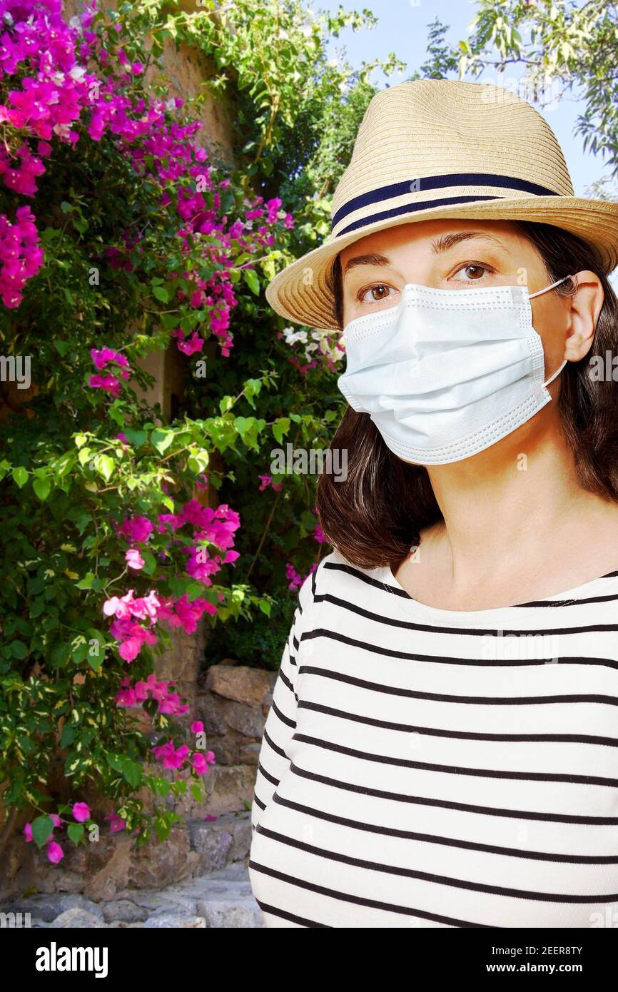 Reisen zu einem mediterranen Ziel während der Corona oder covid Pandemie: Frau Tourist mit einem Sonnenhut und medizinische Gesichtsmaske. Stockfoto