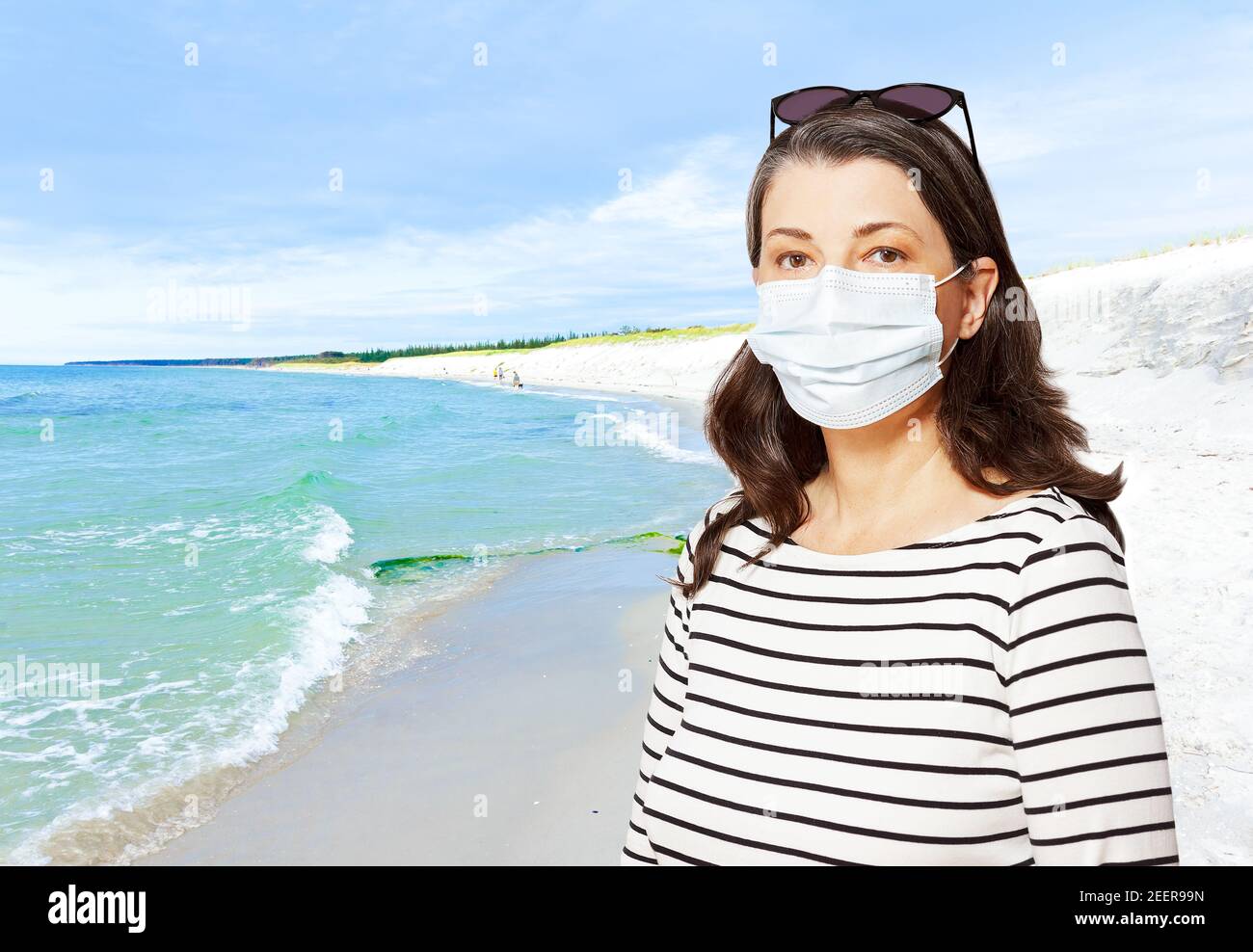Reisen während der Coronavirus-Pandemie: Frau Tourist mit einer Sonnenbrille und medizinische Gesichtsmaske, vor einem Strand. Stockfoto