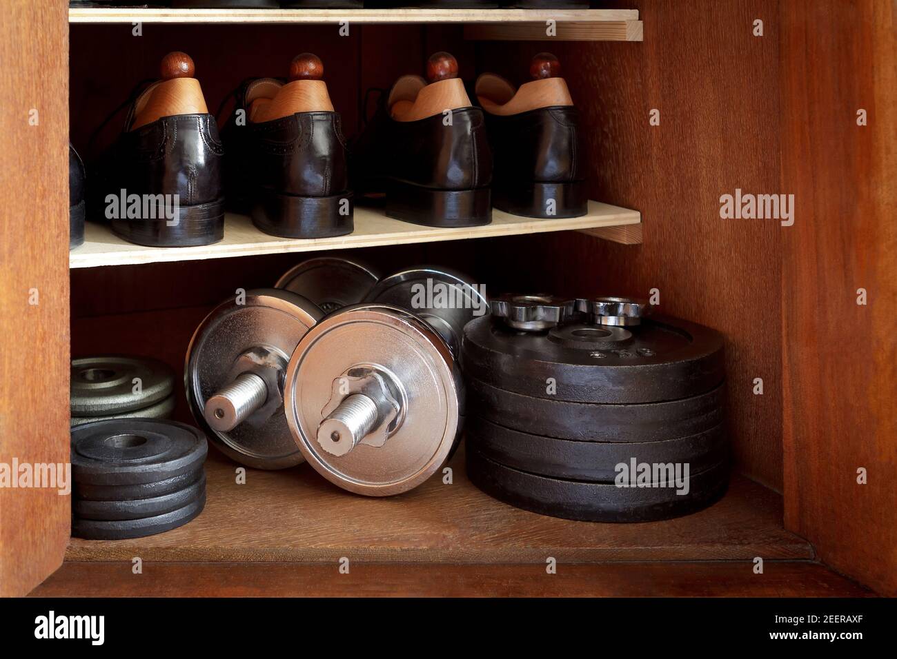 Covid Heimfitness: Bügeln Sie Hanteln und Gewichte unter schwarzen Schuhen unten in einem Kleiderschrank oder Schrank. Stockfoto