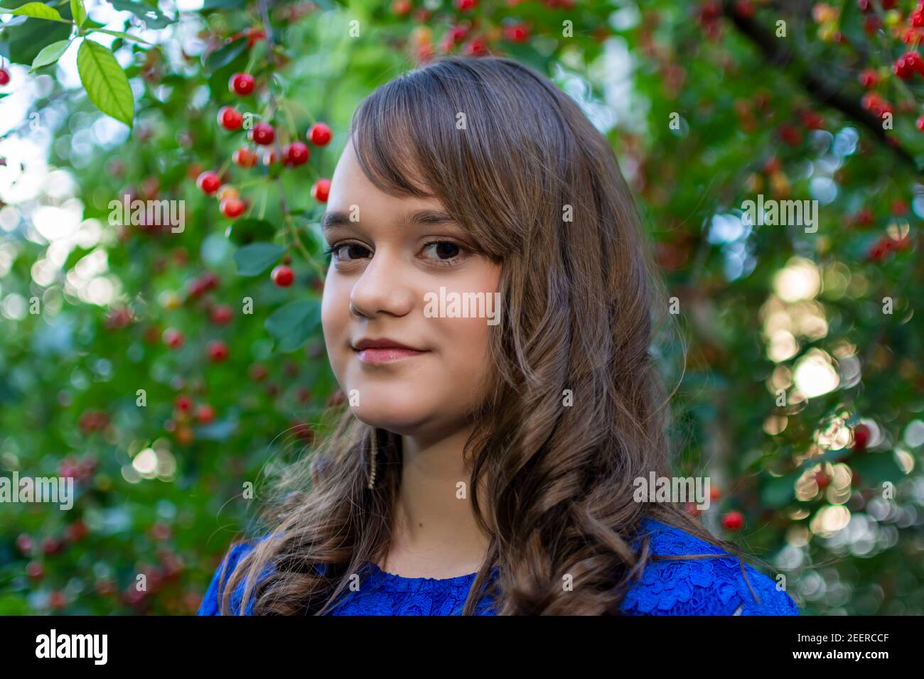 Hübsches Mädchen lächelt während der Aufnahme Foto in Kirschgarten. Portrait von jungen Mädchen mit Make-up. Reife Kirschfrüchte im Hintergrund. Für den Sommer Stockfoto