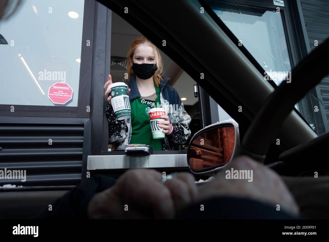 Ein maskierter Starbucks Barista, der einem Gast während der Pandemie von Covid durch das Drive-Thru-Fenster Kaffee überreicht. St. Paul Minnesota, USA Stockfoto