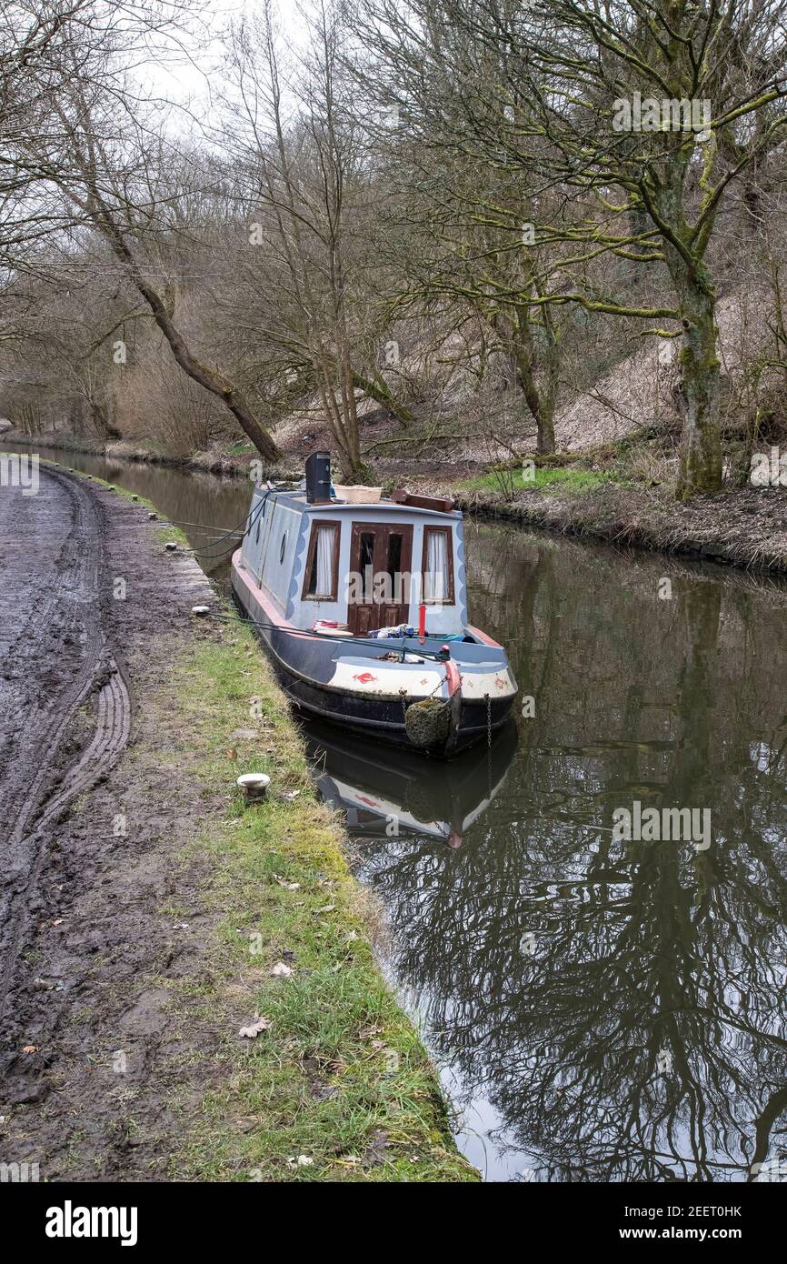Ein alterndes schmales Boot wird im Winter entlang eines schlammigen Treidelpfads auf dem Huddersfield Narrow Canal westlich von Slaithwaite Dorf in Yorkshire U.K. gebunden Stockfoto
