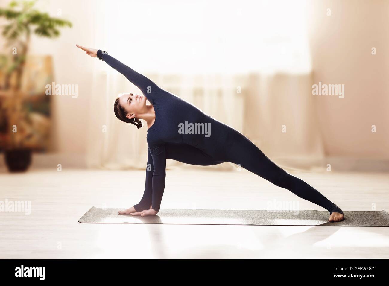 Frau in blauer Sportkleidung Yoga üben, tun uttkhita parshvakonasana Übung in einer Wohnung in der Nähe des Fensters Stockfoto