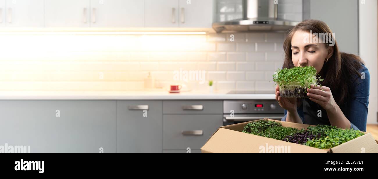 Bio roh Microgreens - Banner einer Frau, die einen Behälter mit Sprossen vor ihrem Gesicht mit geschlossenen Augen hält. Karton mit mehrfachem Sprossen Stockfoto
