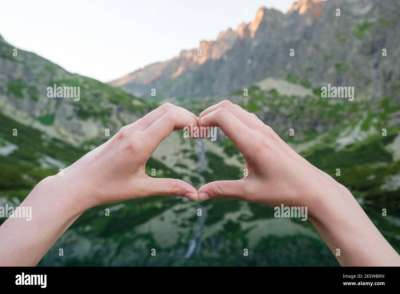 Frauen, die mit ihren Händen Herzform gegen die Berge nahe dem See Formen. Stockfoto