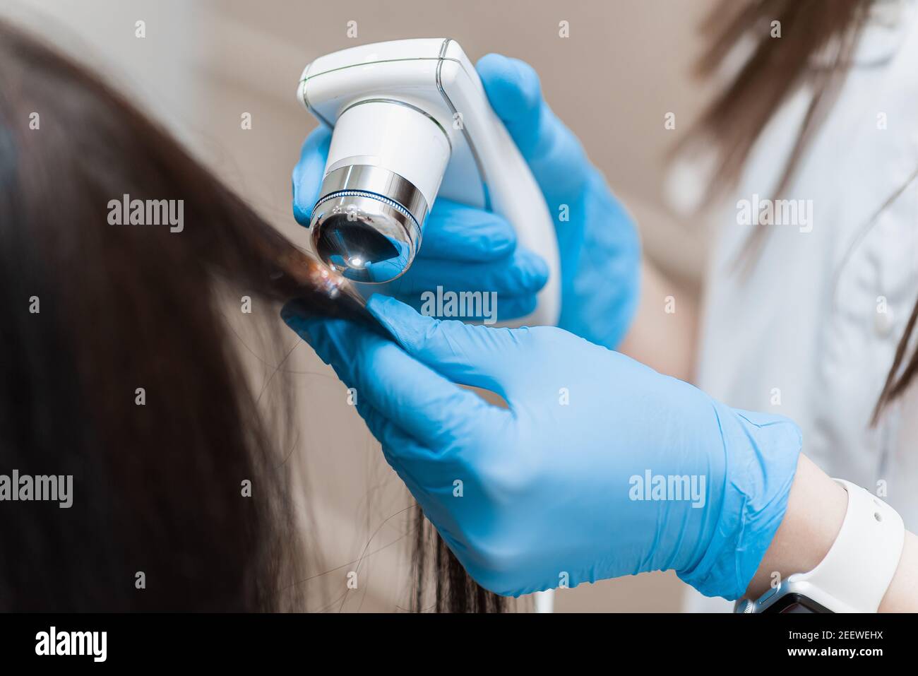 Ein Trichologe mit einem Trichoskop untersucht das lange Haar eines Mädchens Stockfoto