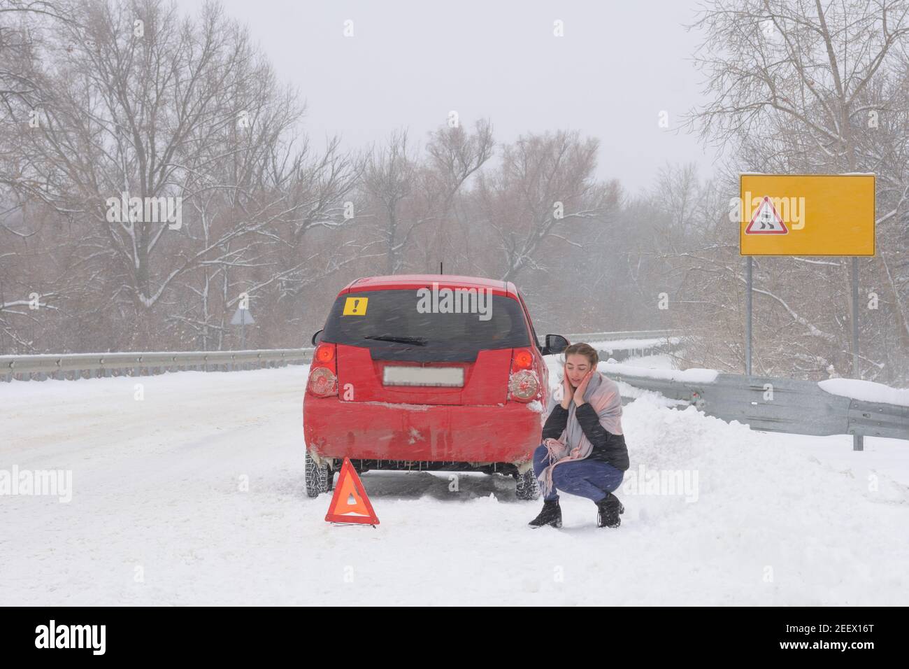 Panne auf der Strecke bei Schneesturm und schlechtem Wetter. Frau Fahrer ohne Erfahrung sitzt und sorgt sich in der Nähe dreieckigen Unfallschild. Stockfoto
