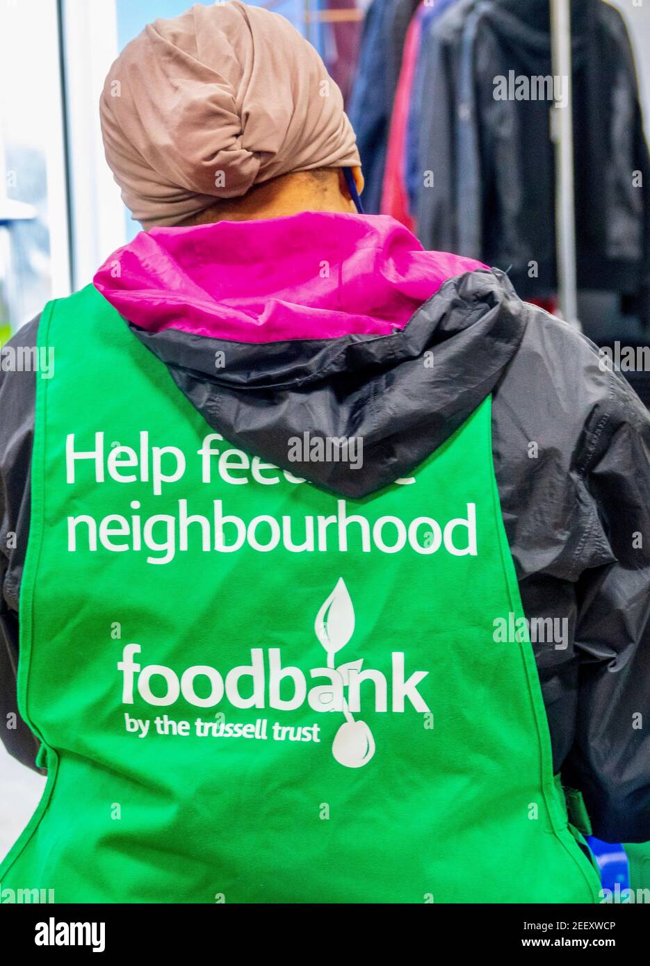 Ein Trussell Trust Foodbank Freiwilliger trägt eine grüne Schürze. Eine asiatische Frau mit Kopftuch, die sich freiwillig für die Bekämpfung der Lebensmittelarmut in London engagiert. VEREINIGTES KÖNIGREICH Stockfoto