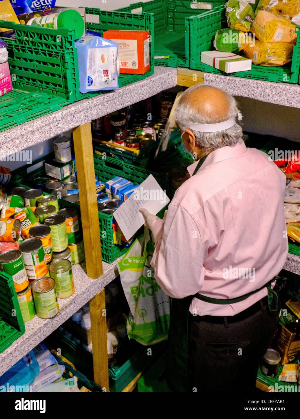 Ein älterer Mann, der einen Gesichtsschutz trägt, sammelt freiwillig Lebensmittel aus der Speisekammer und dem Vorratsschrank einer Trussell Trust Foodbank, um Kunden in Großbritannien zu geben Stockfoto