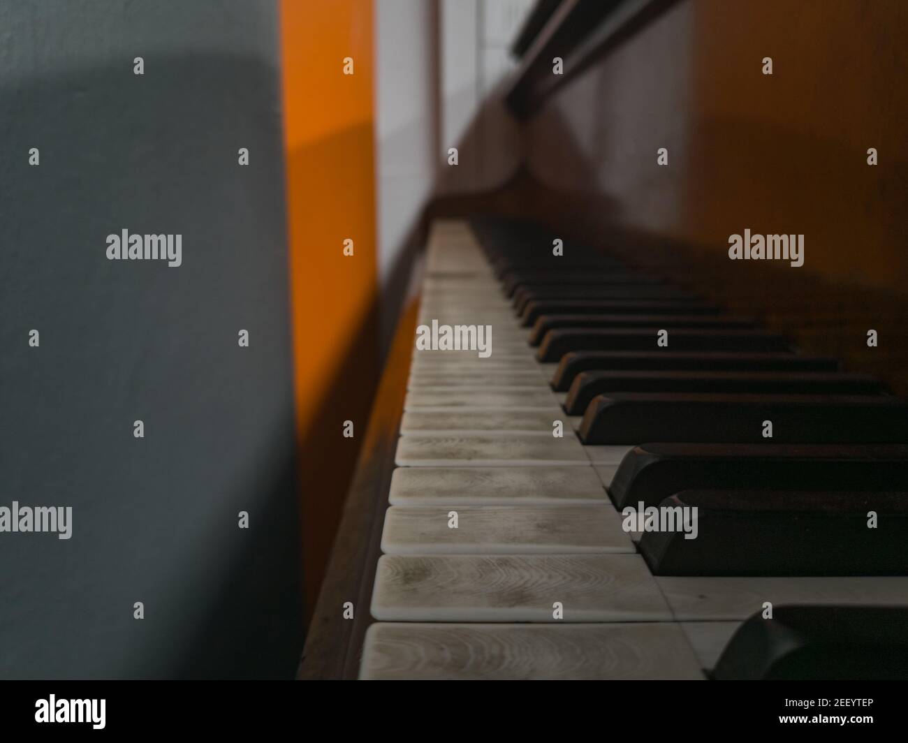 Altes, ungenutztes Klavier, das neben einer grauen und orangen Wand steht Stockfoto