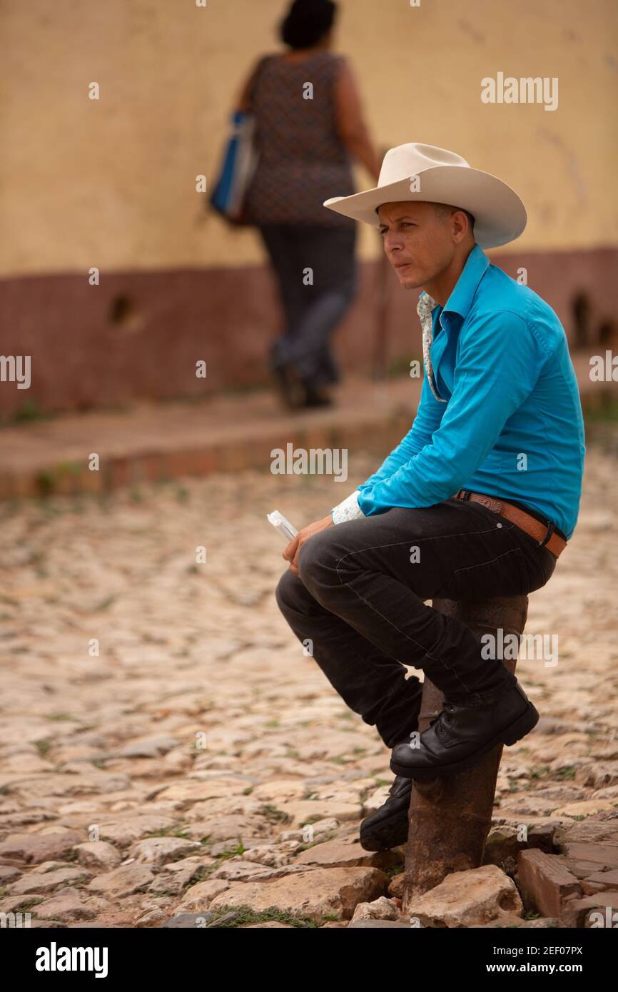 Ein junger Mann in Cowboyhut, leuchtend blauem Hemd und schwarzen Stiefeln wartet auf den Straßen von Trinidad in Kuba Stockfoto