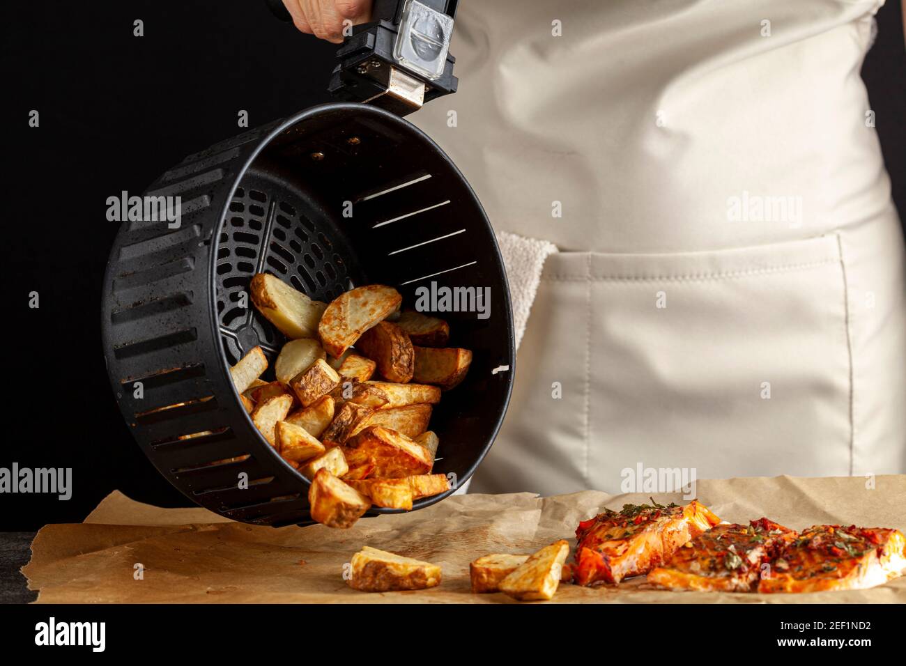 Eine kaukasische Köchin dumpt frisch gebackene Bratkartoffeln Brocken auf einem Stück Backpapier, das drei hat Im Ofen geröstetes mariniertes Lachsfilet mit Stockfoto
