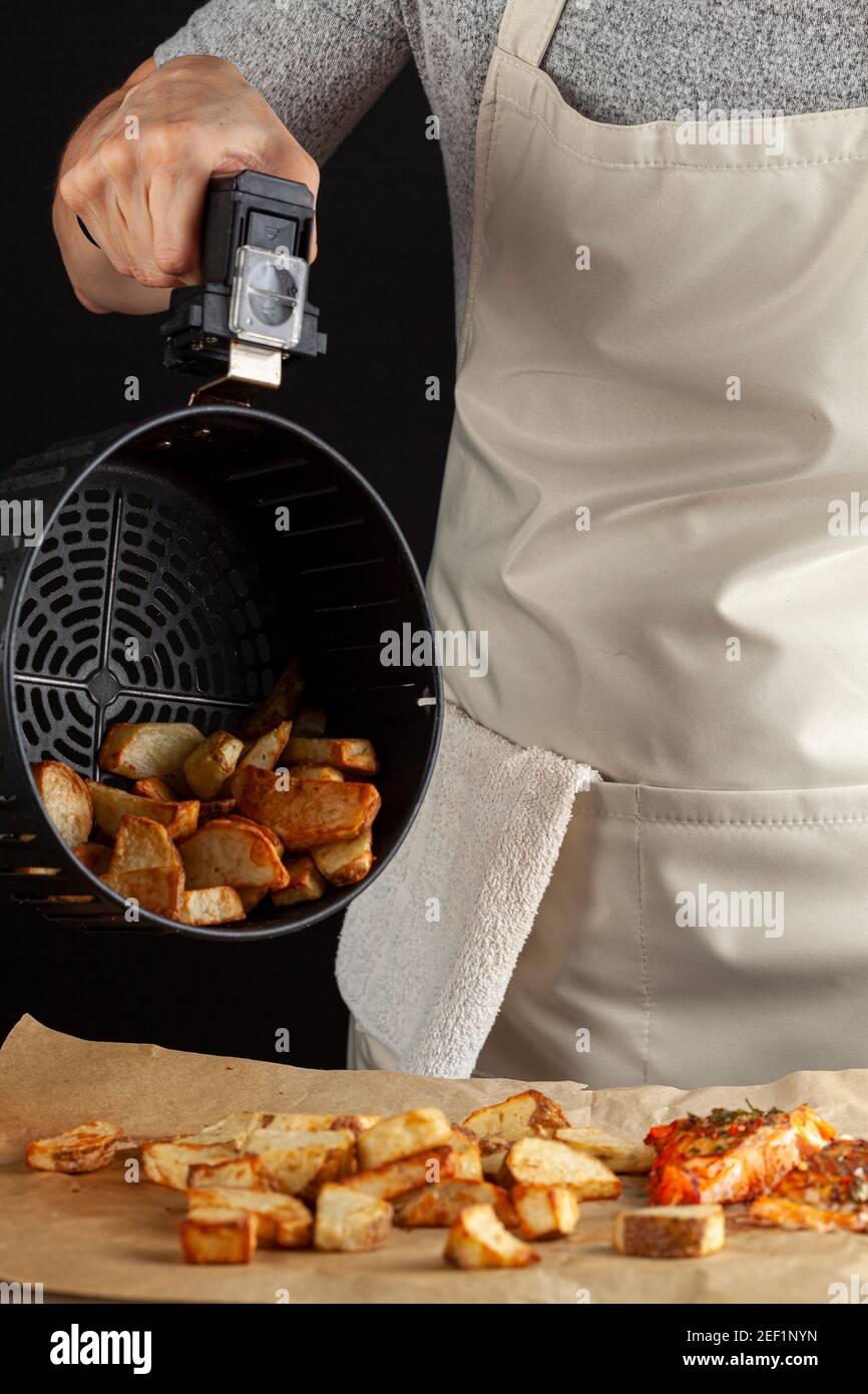 Eine kaukasische Köchin dumpt frisch gebackene Bratkartoffeln Brocken auf einem Stück Backpapier, das drei hat Im Ofen geröstetes mariniertes Lachsfilet mit Stockfoto