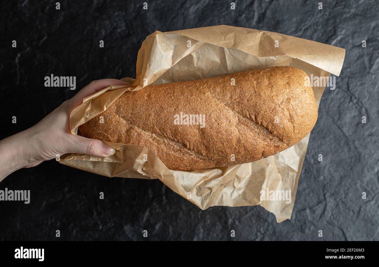 Frau Auspacken mit ihren Händen Brot Papier auf schwarzem Hintergrund Stockfoto