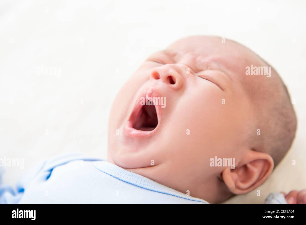 Schläfrig liebenswert neugeborenes Baby im Bett liegen und gähnend - Weichfokus Stockfoto